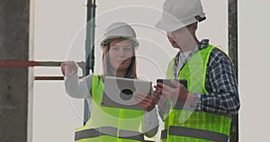 Building in construction with a female and a male engineers using a tablet and mobile phone to visualize the building