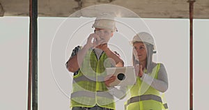 Building in construction with a female and a male engineers using a tablet and mobile phone to visualize the building