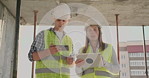 Building in construction with a female and a male engineers using a tablet and mobile phone to visualize the building