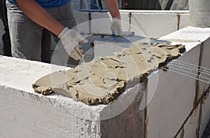 A building contractor is applying a generous amount of mortar with a spade mortar to bricklaying a wall of a new house