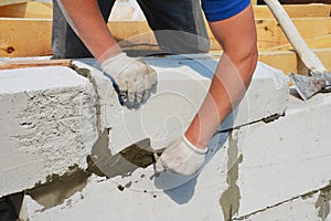A building contractor is constructing a wall from autoclaved aerated concrete blocks using a trowel and an axe, attaching concrete
