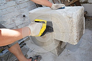 A building contractor is cutting autoclaved aerated concrete block, gas concrete using a hand saw on a construction site