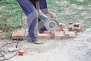 A building contractor is cutting bricks with an angle grinder or disc grinder