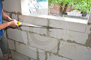 A building contractor is cutting the wall with a masonry brick block cutting hand saw to enlarge a window opening