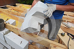 A building contractor installing an autoclaved aerated concrete block of irregular form, cut by a handsaw to lay it on the edge of