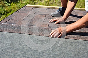 A building contractor is installing  dimensional asphalt roof shingles on the underlayment of the house construction repairing the