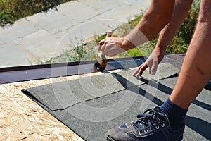 A building contractor is installing underlayment, a layer of bitumen tape on sheathing for overall roof protection at the ridge of