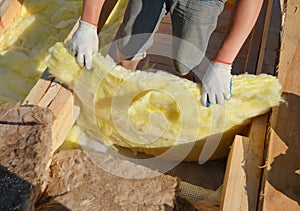 A building contractor is laying mineral wool sheets in protective gloves on the rooftop for thermal insulation, energy efficiency