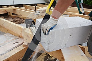 A building contractor in protective gloves is cutting an autoclaved aerated concrete block using a hand saw
