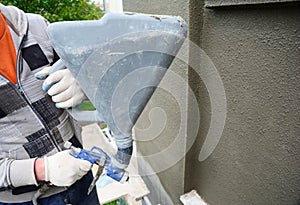 A building contractor is renovating, rendering exterior walls of the house, applying stucco, spaying texture using a texture air