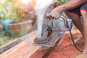 Building contractor worker using hand held worm drive circular saw to cut boards on a new home constructiion project