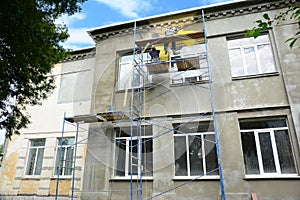 Building contractors on scaffoldings are plastering, rendering the facade of a building using plastic and fiberglass mesh as a