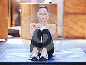 Building core strength and stability. Portrait of a sporty young woman doing sit ups while exercising in a gym.