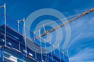 Building and crane jib surrounded by scaffolding scaffolding and netting