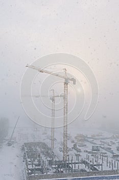 Building cranes on the construction site during snowfall in winter