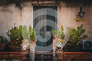Building exterior wall with door and wooden green shade. Patio with brick wall and Taormina decoration heads with plants