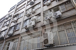 a building facade in bad condition with bars on the windows and with many air conditioners hanging up, a feeling of overwhelm and