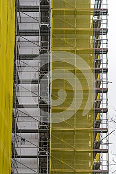 Building facade renovation, old house reconstruction, repair. Scaffold in front of building facade covered with yellow transparent