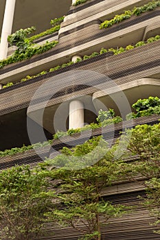 A building features concrete levels lined with various plants and greenery. Sunlight shines on the structure, highlighting the mix