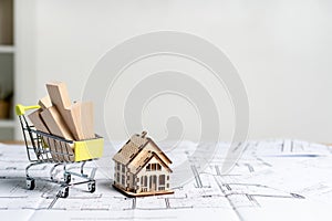 Building flat and apartment in new house concept. Little wooden house standing near small shopping cart with building materials on