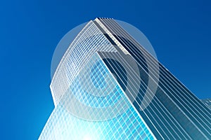 Building of a glass skyscraper with a blue flare against the sun against a blue sky.