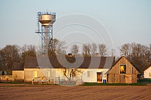 The building of a livestock farm, a water tower and a plowed field during sunset. An agricultural field on the territory of an