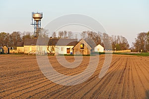 The building of a livestock farm, a water tower and a plowed field during sunset. An agricultural field on the territory of an