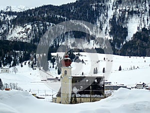 The building of the old church in the snow at the foot of the winter forested mountains