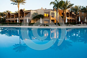 Building reflection on swimming pool water. Evening sun on building with two palms reflect to water mirror.