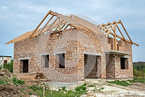 Building site with unfinished brick house with wooden roofing frame for future roof under construction