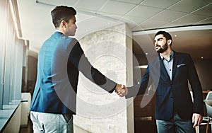 Building solid relationships with clients is critical for success. two young businessmen shaking hands in a modern