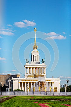 A building with a spire of white columns and statues against a blue sky background.