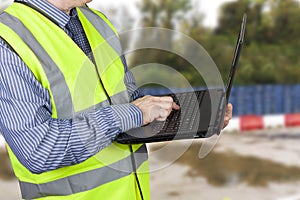 Building surveyor in hi vis vest entering data into his laptop