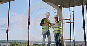 Building technology and people concept - smiling builders in hardhats with tablet pc computer outdoors.