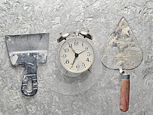Building tools on a gray concrete background. Spatula, trowel, alarm clock, top view.