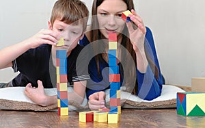 Building a towers from blocks. Mom and son playing together with wooden colored education toy blocks lying on the floor.