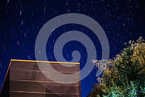 Building and tree in front of star trails