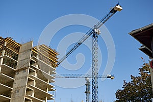 A building under construction and a construction crane against a blue sky on a bright sunny day.