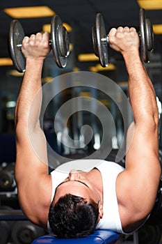 Building upper body strength. A young man lifting weights on a bench.