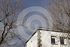 Building. White colored building next to some bare and leafless trees in the surroundings.