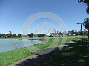 Buildings and amusement park in the background, plants, lake, flowers, trees and concrete walking path in Barigui park photo