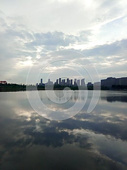 Buildings and clouds reflected in calm lake. Reflection mirror in city