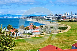 Buildings on edge of beach with people on trail and distant San Francisco skyscrapers and bridge