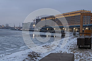 Buildings on the embankment, frozen Neva River, parked cars, a boat. St. Petersburg, the beginning of winter.