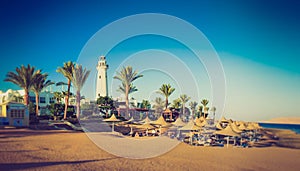 Buildings of the luxury hotel and palm alley on egyptian beach, lighthouse. Red Sea. Egypt.