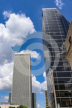 Buildings of modern city jutting up into intensely blue clouded sky with reflections