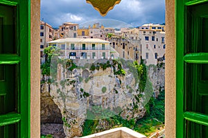 Buildings on stone rock cliff in Tropea town historical centre, view through window of Monastery Sanctuary church