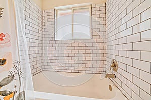 Built in bathtub inside bathroom with white tiles on wall and sliding window