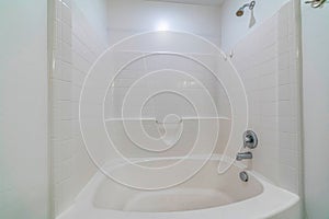 Built in bathtub with shower inside a bathroom with shiny clean white tiles