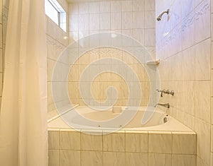 Built in bathtub and shower inside a bathroom with shiny wall and small window